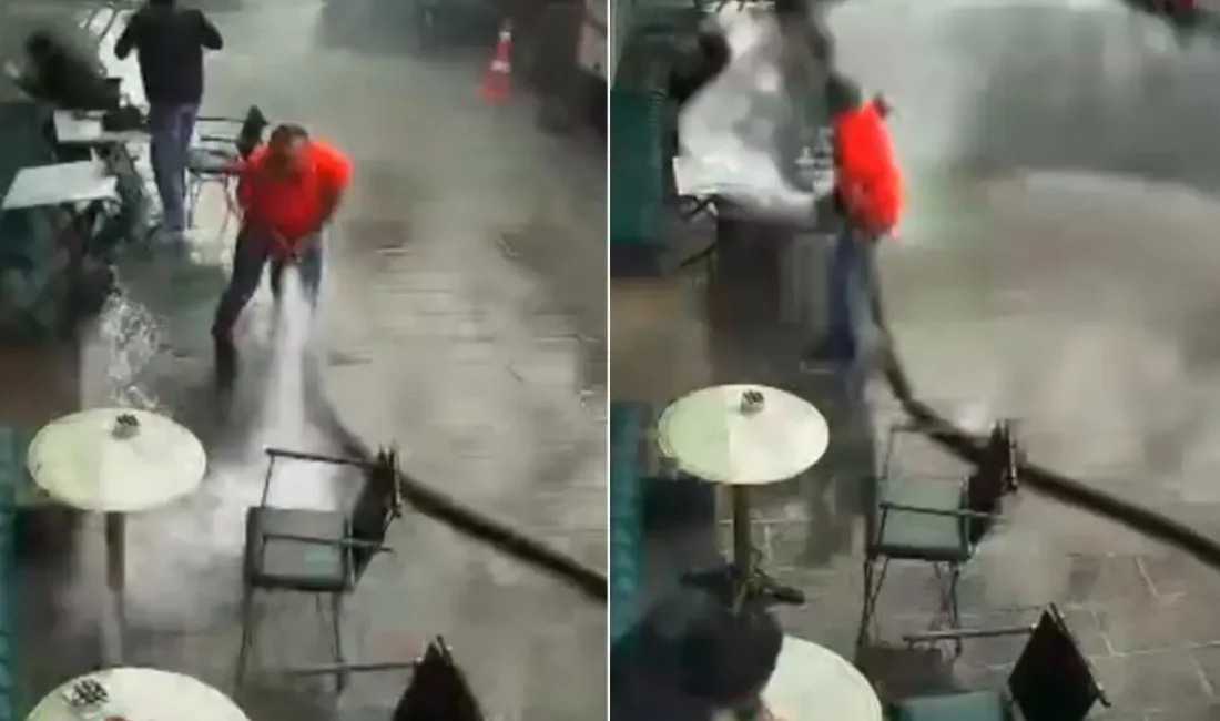 Bir kafe işletmecisi, iş yerinin önünü tazyikli suyla temizlemeye çalışırken