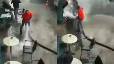 Bir kafe işletmecisi, iş yerinin önünü tazyikli suyla temizlemeye çalışırken