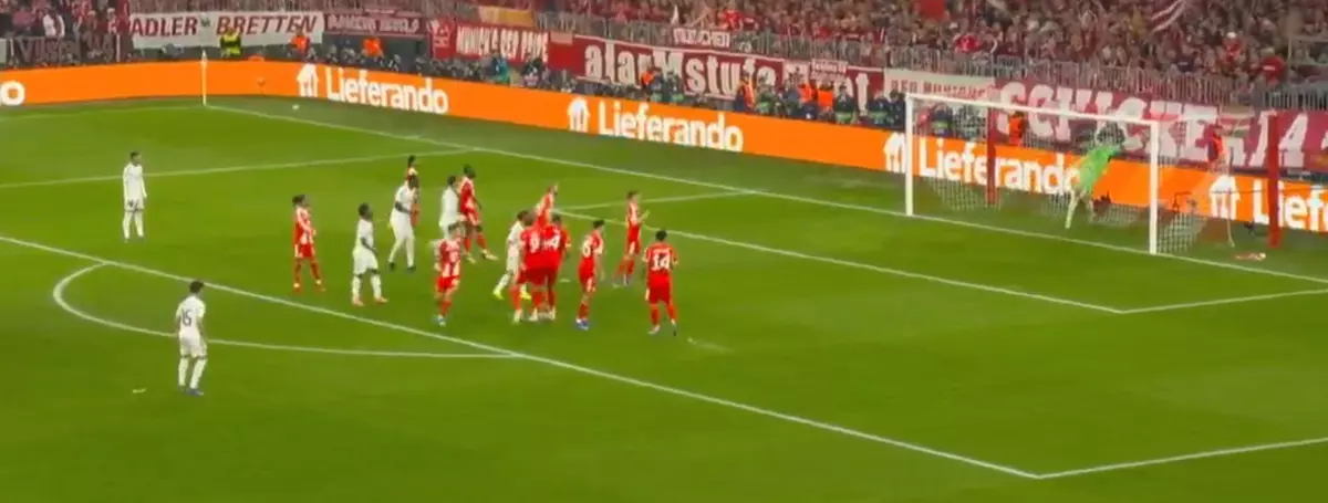 Soccer players in red and white battle near the goal during a set-piece as fans watch from the stands.
