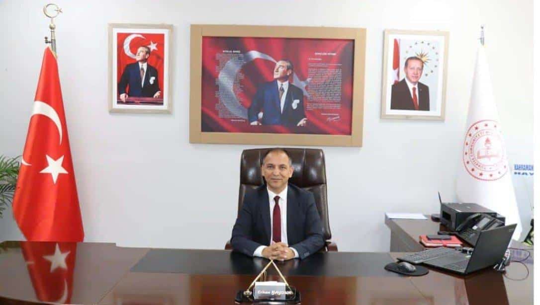 Man in a suit sits at a large desk in a formal office, with a Turkish flag to the left and framed portraits on the wall behind him.