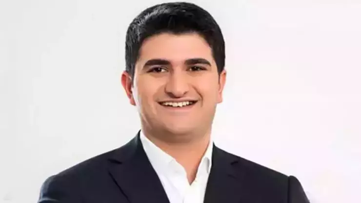 Smiling man in a dark suit and white shirt posing for a headshot against a light background.