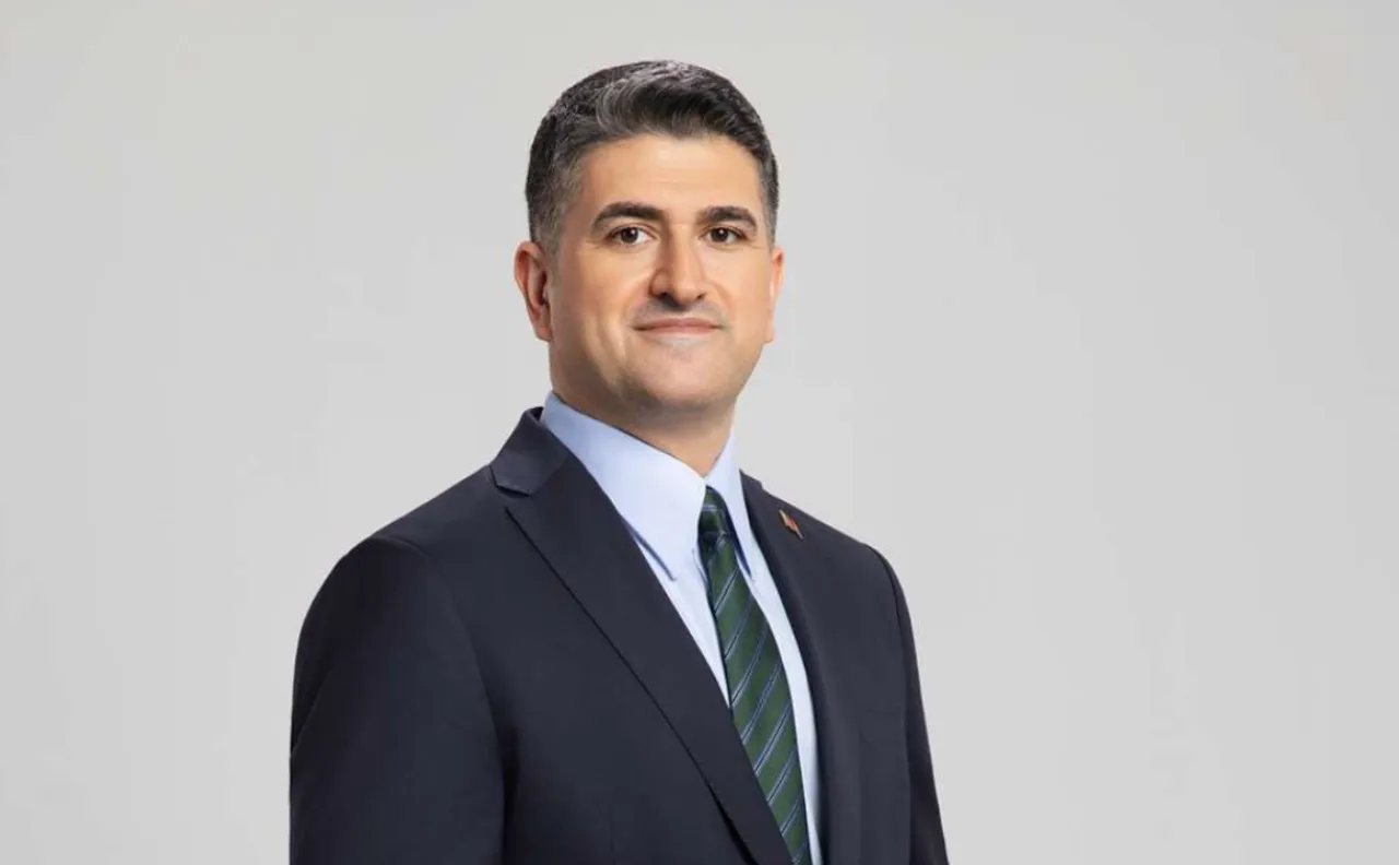 Professional head-and-shoulders portrait of a man in a dark suit, light blue shirt, and green striped tie, facing slightly right with a neutral smile