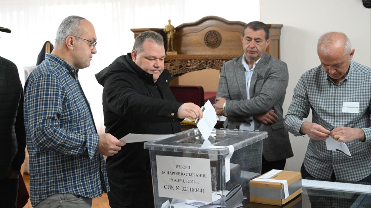 Four men vote at a polling station, placing ballots into a transparent ballot box.