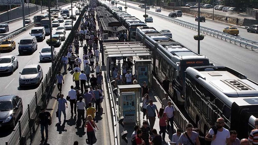 Crowded urban bus stop with a long line of pedestrians on a central platform between lanes of buses and cars on each side.