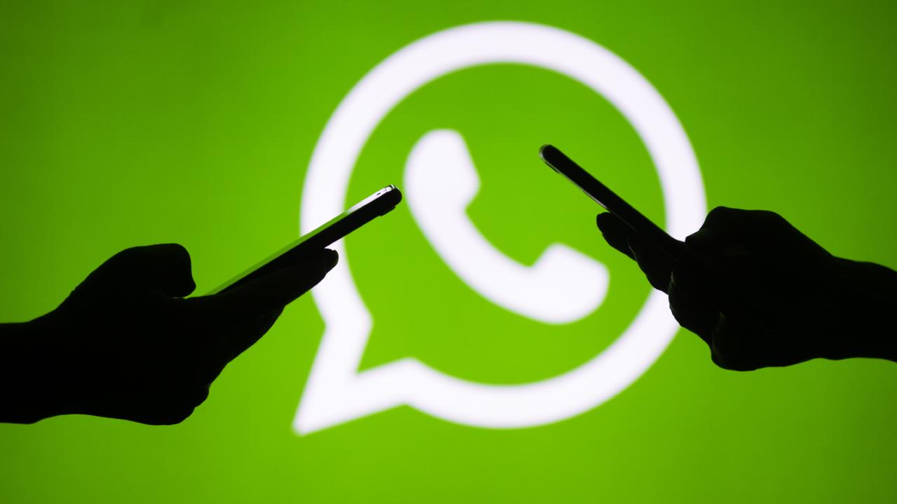 Silhouettes of two people holding smartphones in front of a large white WhatsApp icon on a bright green background.