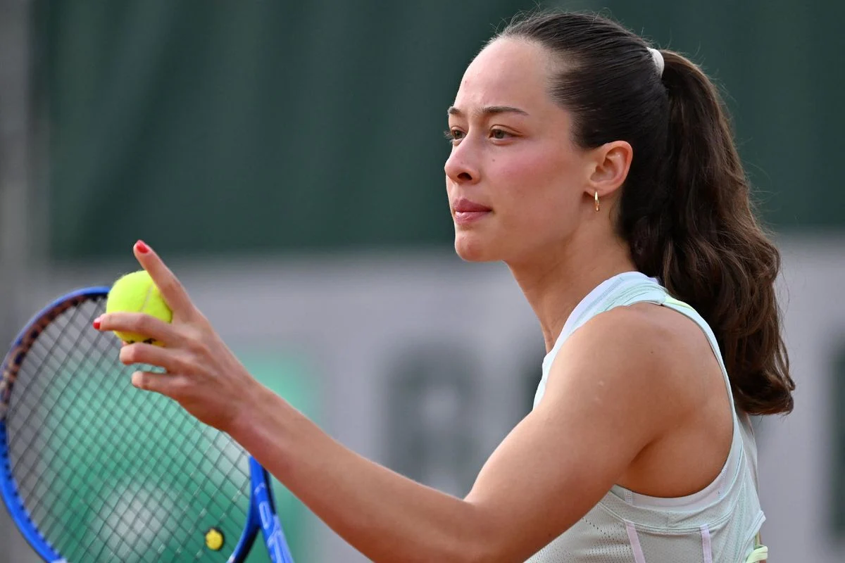 Female tennis player in a white top holds a tennis ball near her racket, focused on the shot on a court.